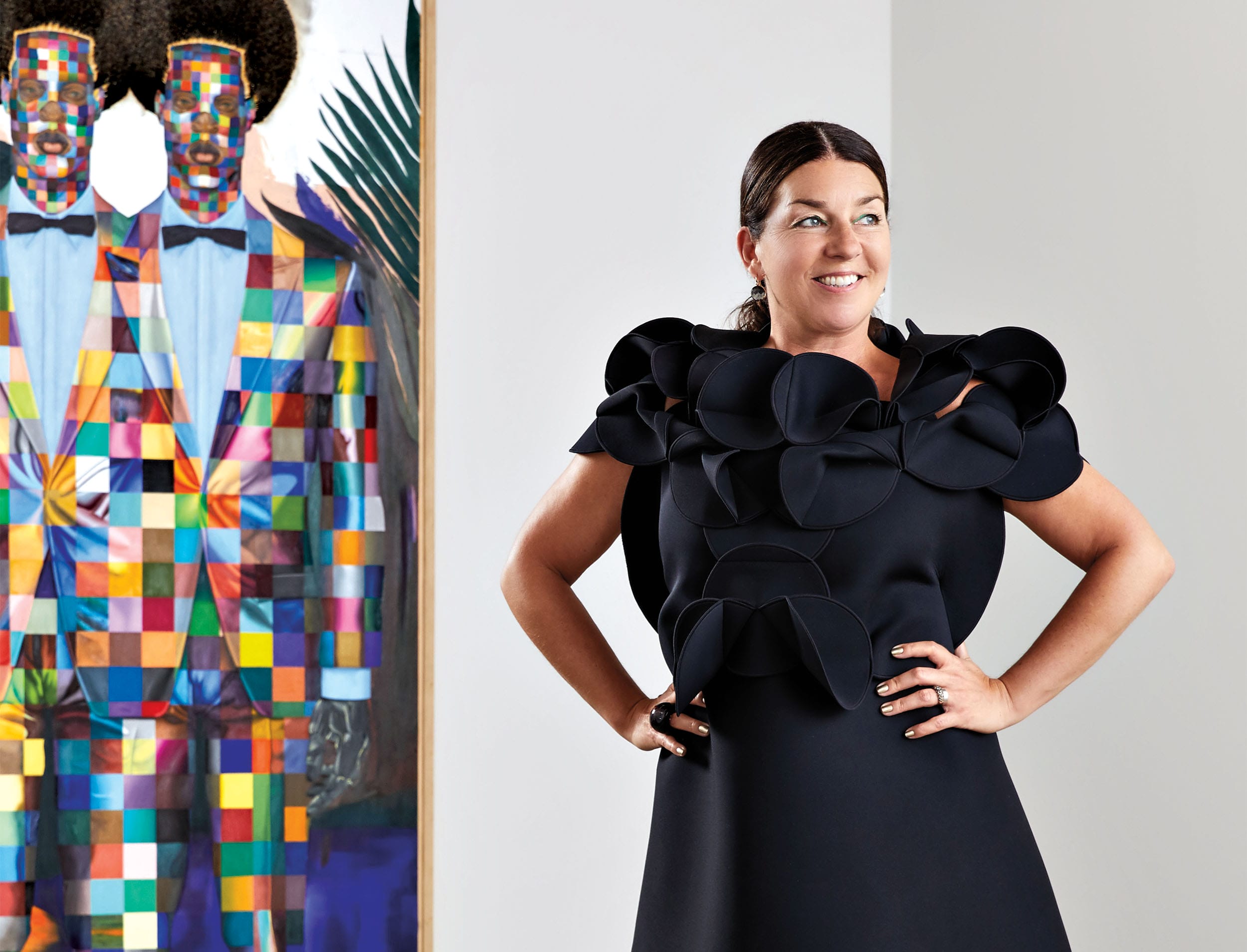 Woman in black dress standing confidently beside colorful abstract artwork featuring two figures in suits.