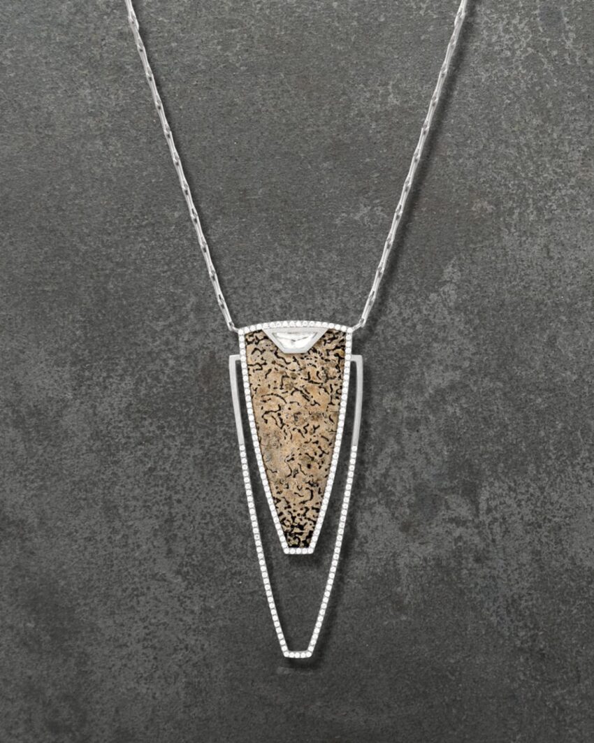 Silver and gold pendant necklace with an intricate design on a textured gray background.