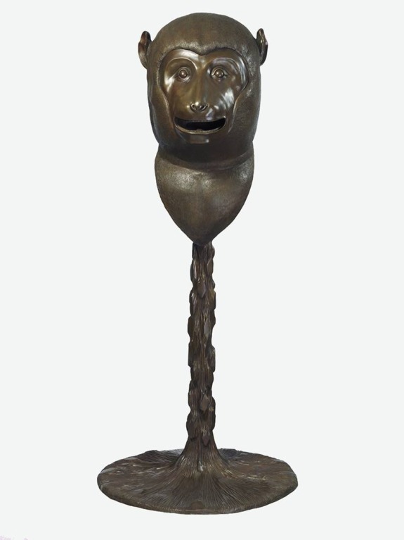 Bronze sculpture of a monkey head on a long textured stem with a round base, blending artistic and animal themes.