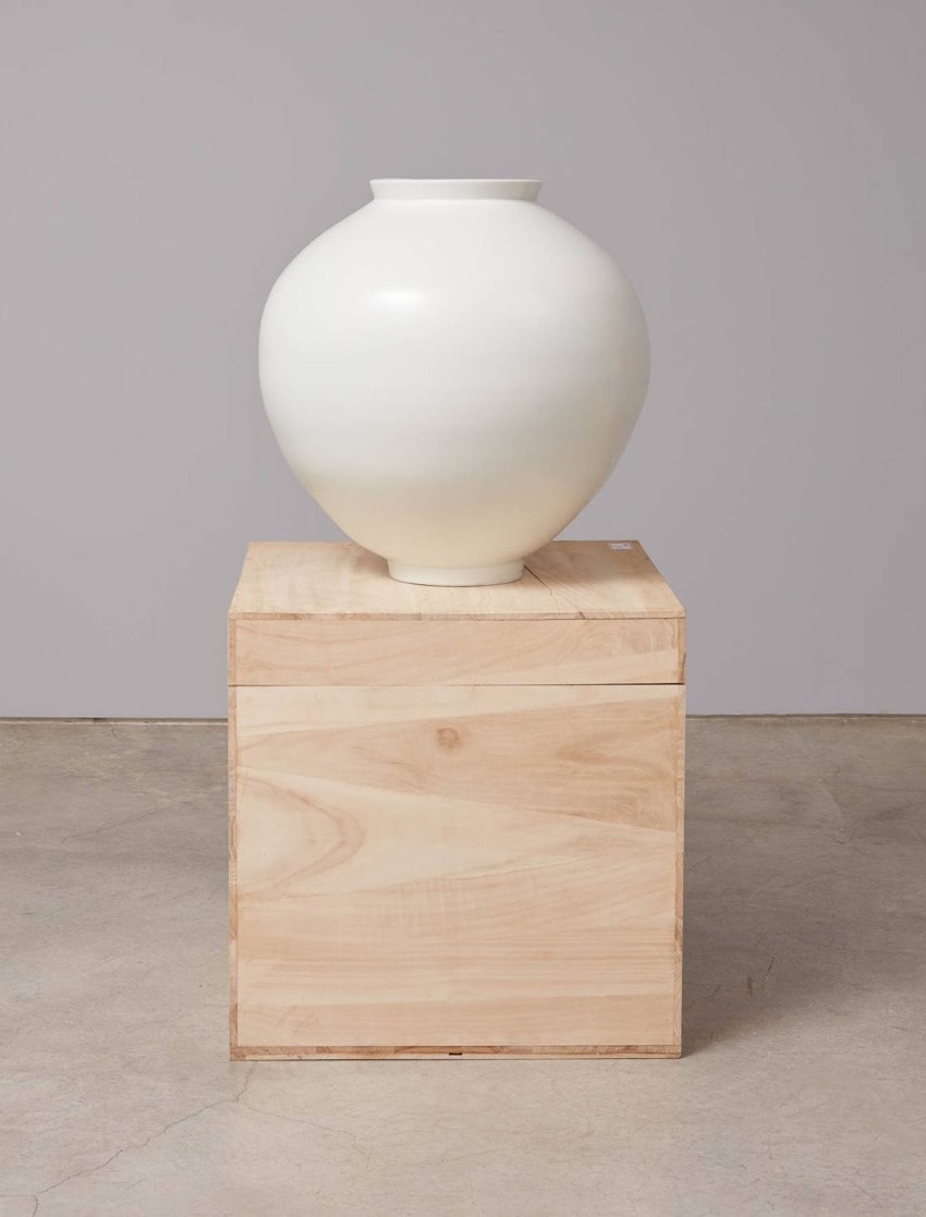 White ceramic vase on a wooden cube stand in a minimalist setting.