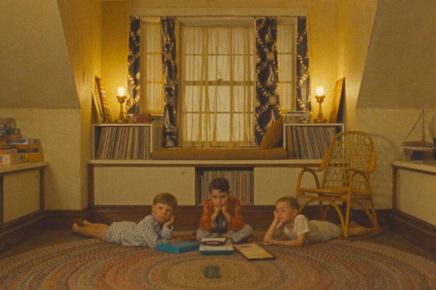 Three children in pajamas lying on the floor reading books in a cozy, dimly lit attic room with games and decor.