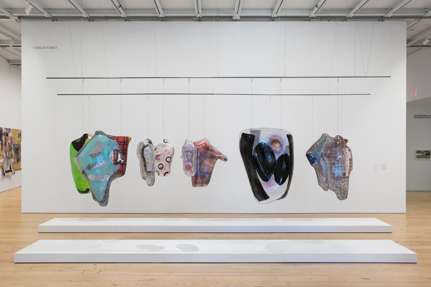 Abstract hanging sculptures displayed in a gallery with a modern design, wooden floors, and white walls.