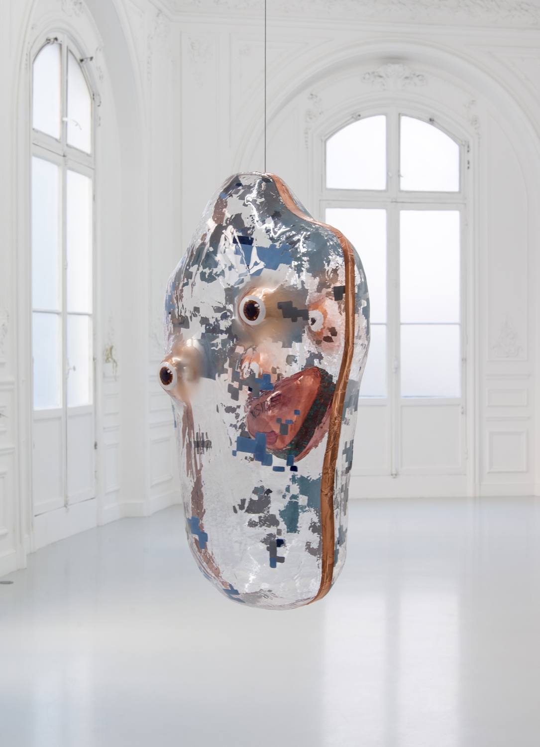 Abstract sculpture hanging in a white room with large windows and intricate molding.