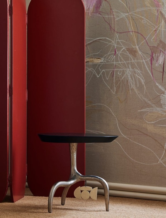 Modern round table with metallic base in front of a red screen and artistic wall mural background.