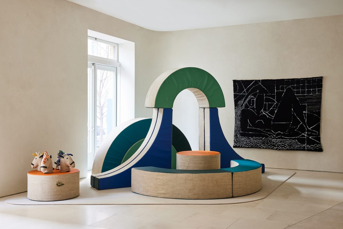 Modern children's play area with an abstract play structure, slide, seating, and colorful stuffed animals on display.