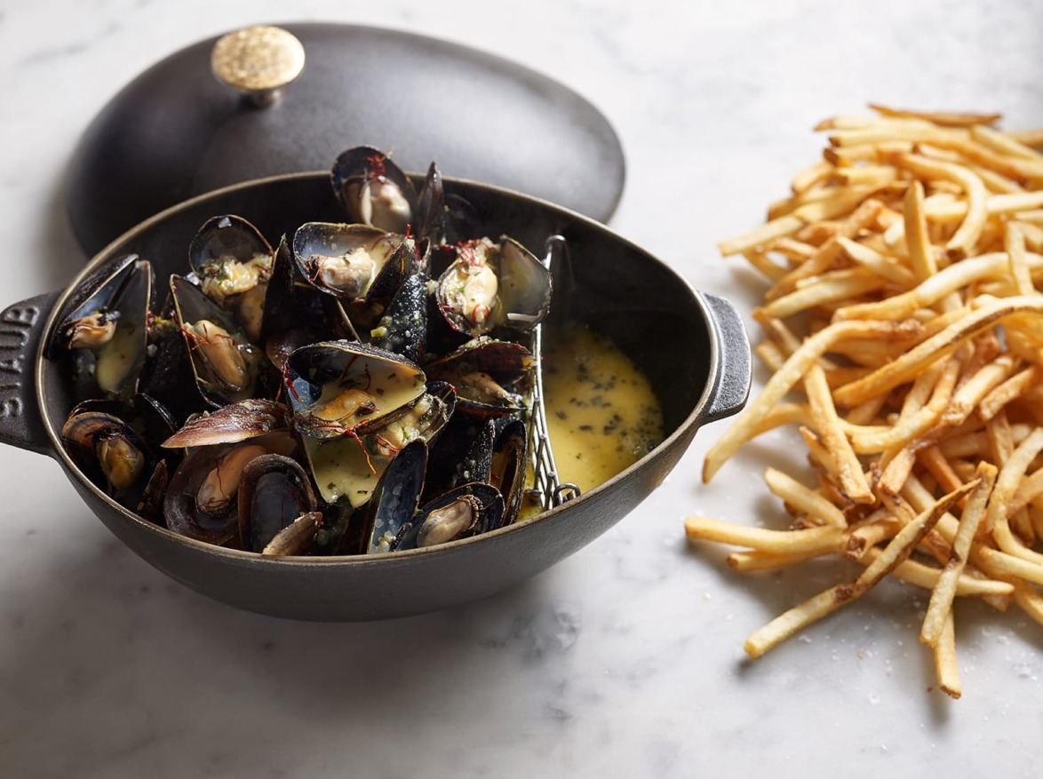 Mussels in a black pot with creamy sauce, served alongside crispy golden fries on a marble surface.