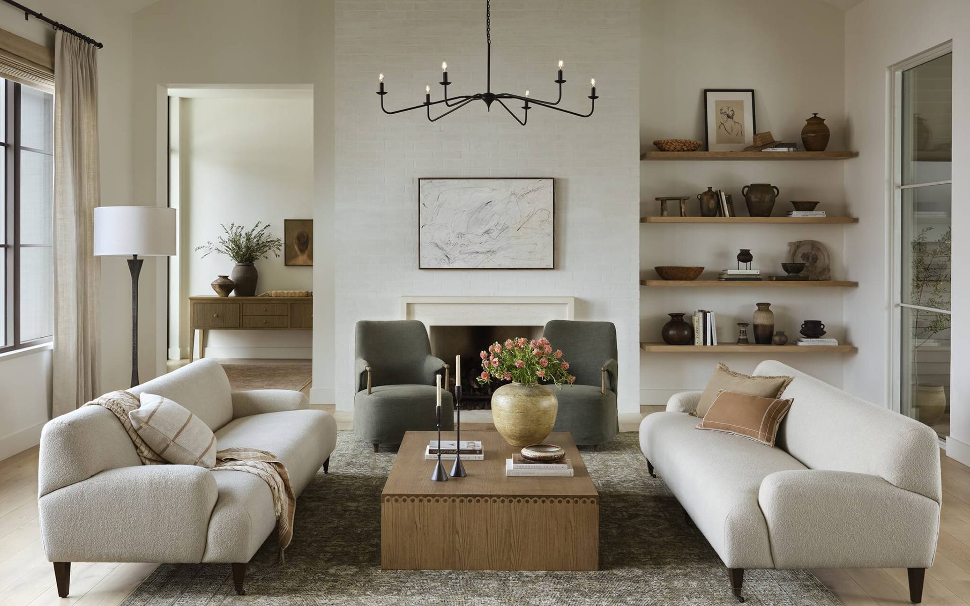 Modern living room with neutral sofas, a wooden coffee table, wall art, and shelves with decorative items on a textured wall.