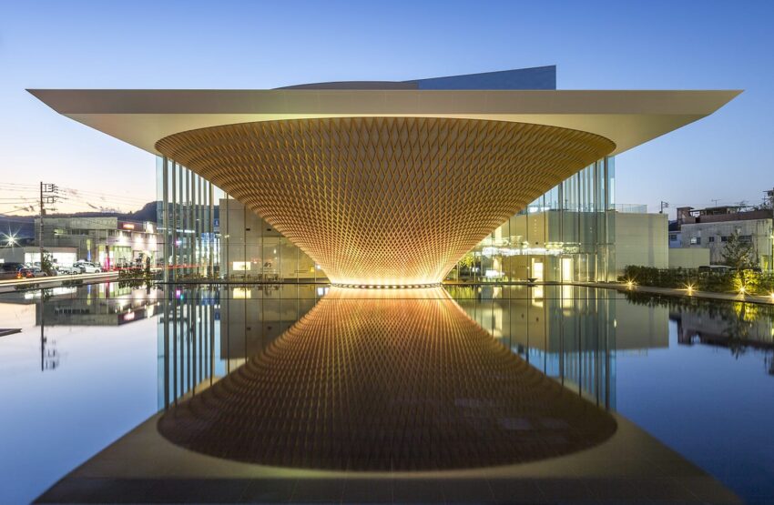 Modern architectural building with a unique curved design, illuminated at night and reflected in a still water surface.