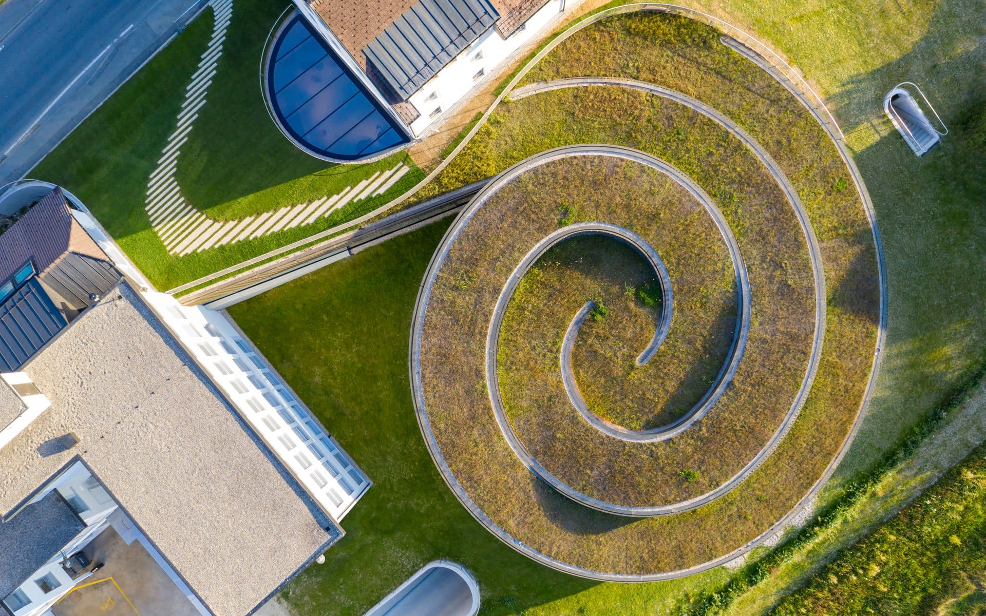 Aerial view of a modern building with a large spiral pathway and green rooftop surrounded by grass.