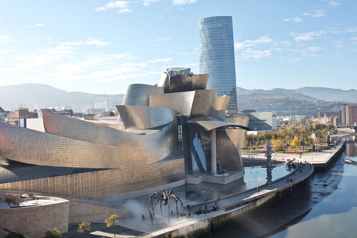 Guggenheim Museum Bilbao with modern architecture and site-specific sculptures along the riverfront and cityscape in the background.