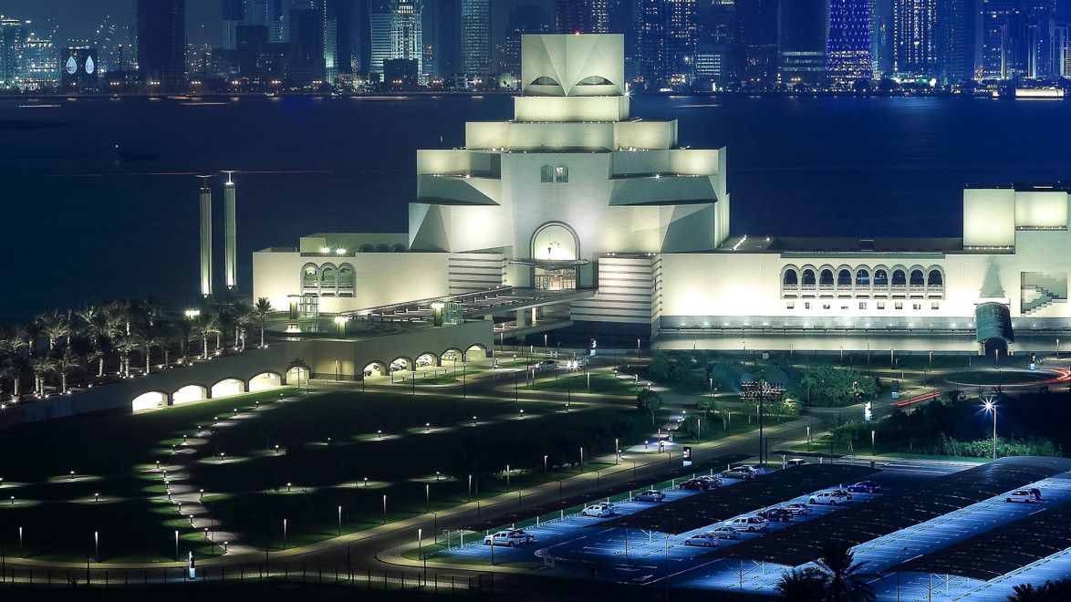Museum of Islamic Art illuminated at night with city skyline in the background, Doha, Qatar.