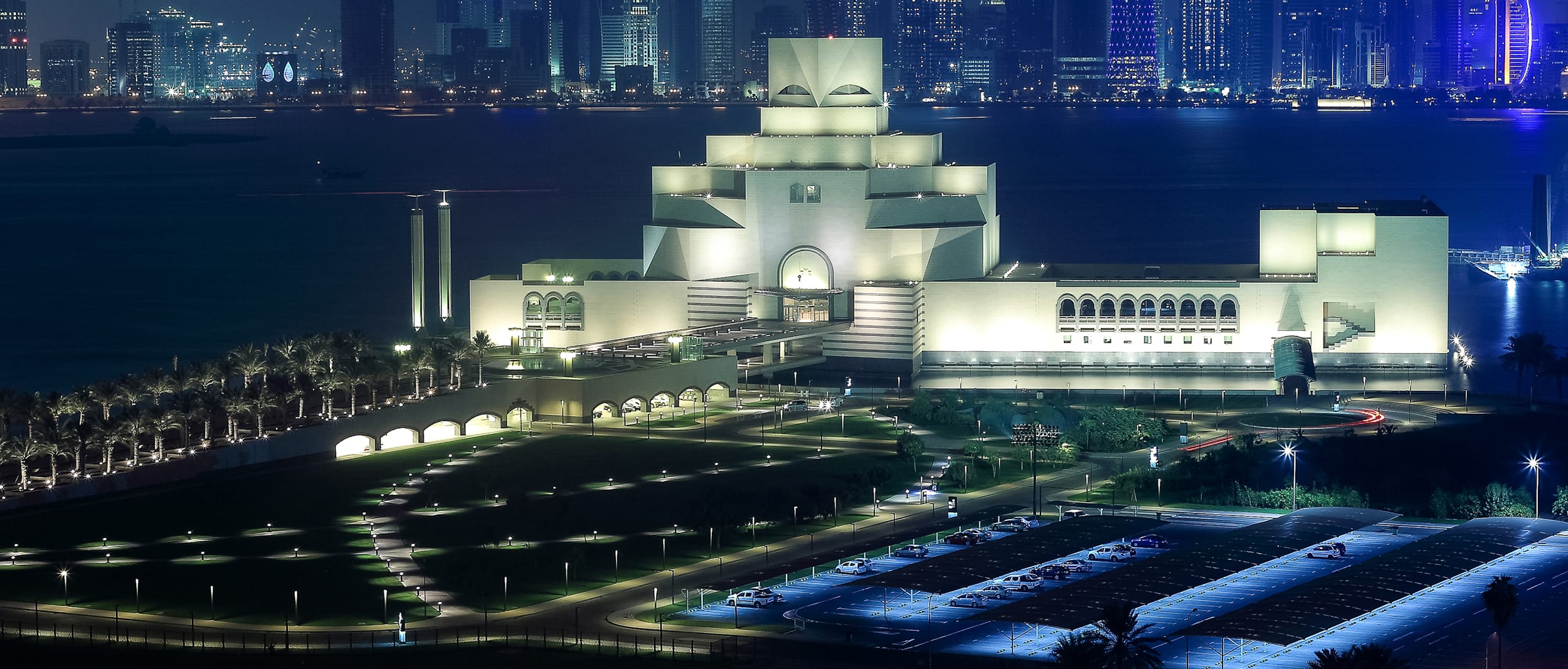 Museum of Islamic Art illuminated at night with city skyline in the background, Doha, Qatar.