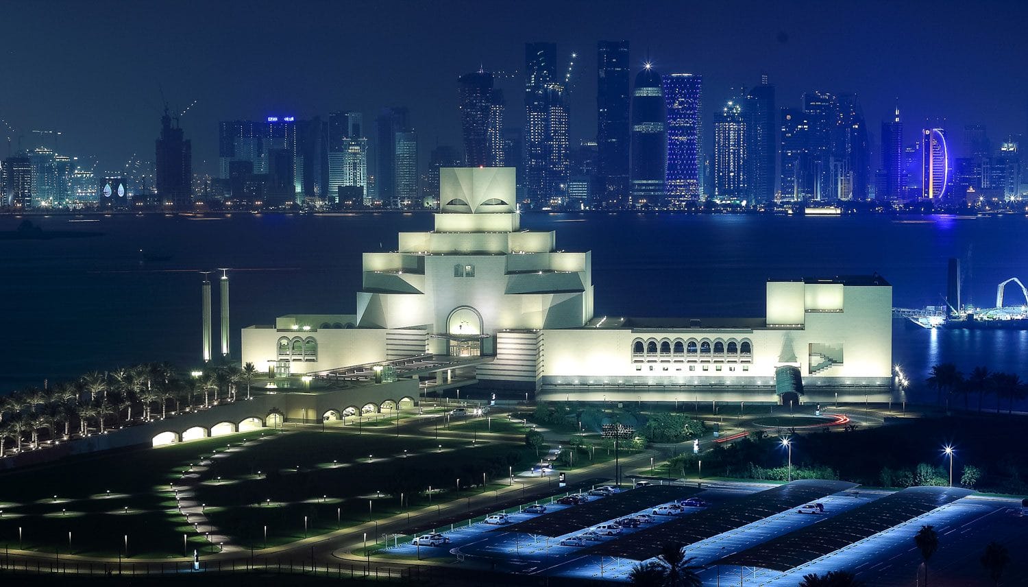 Night view of the Museum of Islamic Art in Doha with city skyline in the background.