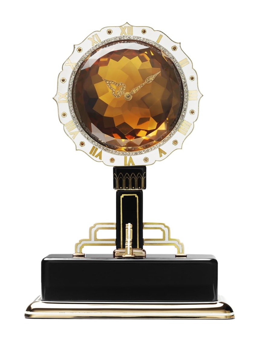 Elegant art deco-style clock with a large amber gemstone face and intricate gold detailing on a black base.