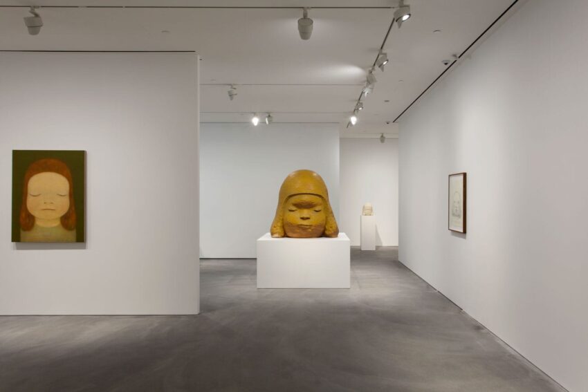 Art gallery interior featuring paintings and a large central sculpture on a pedestal, under spotlights.