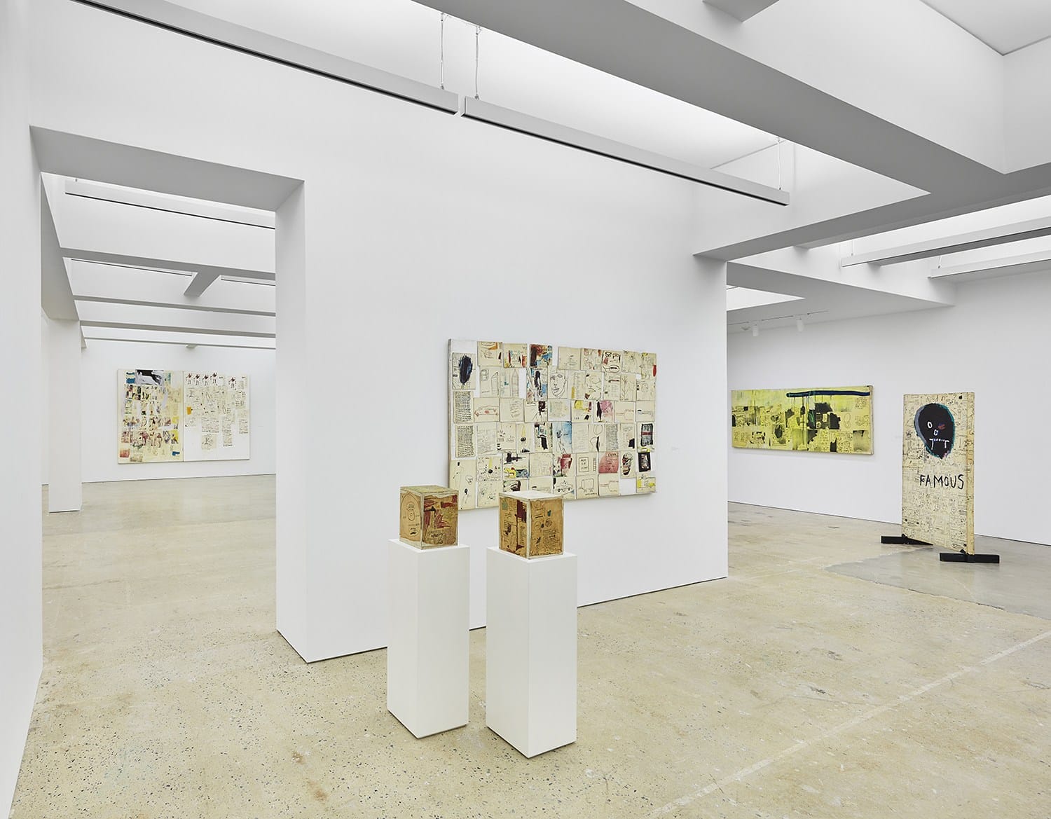 Contemporary art gallery interior with various artworks displayed on white walls and sculptures on white pedestals.