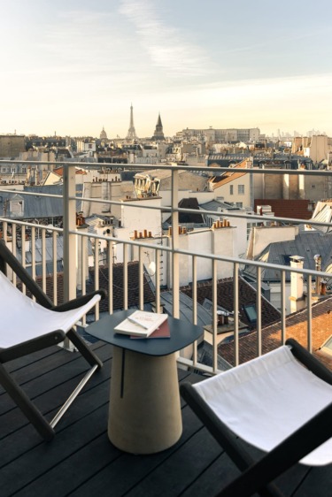 Rooftop view of Paris with Eiffel Tower in the distance, lounge chairs and table on a wooden deck.