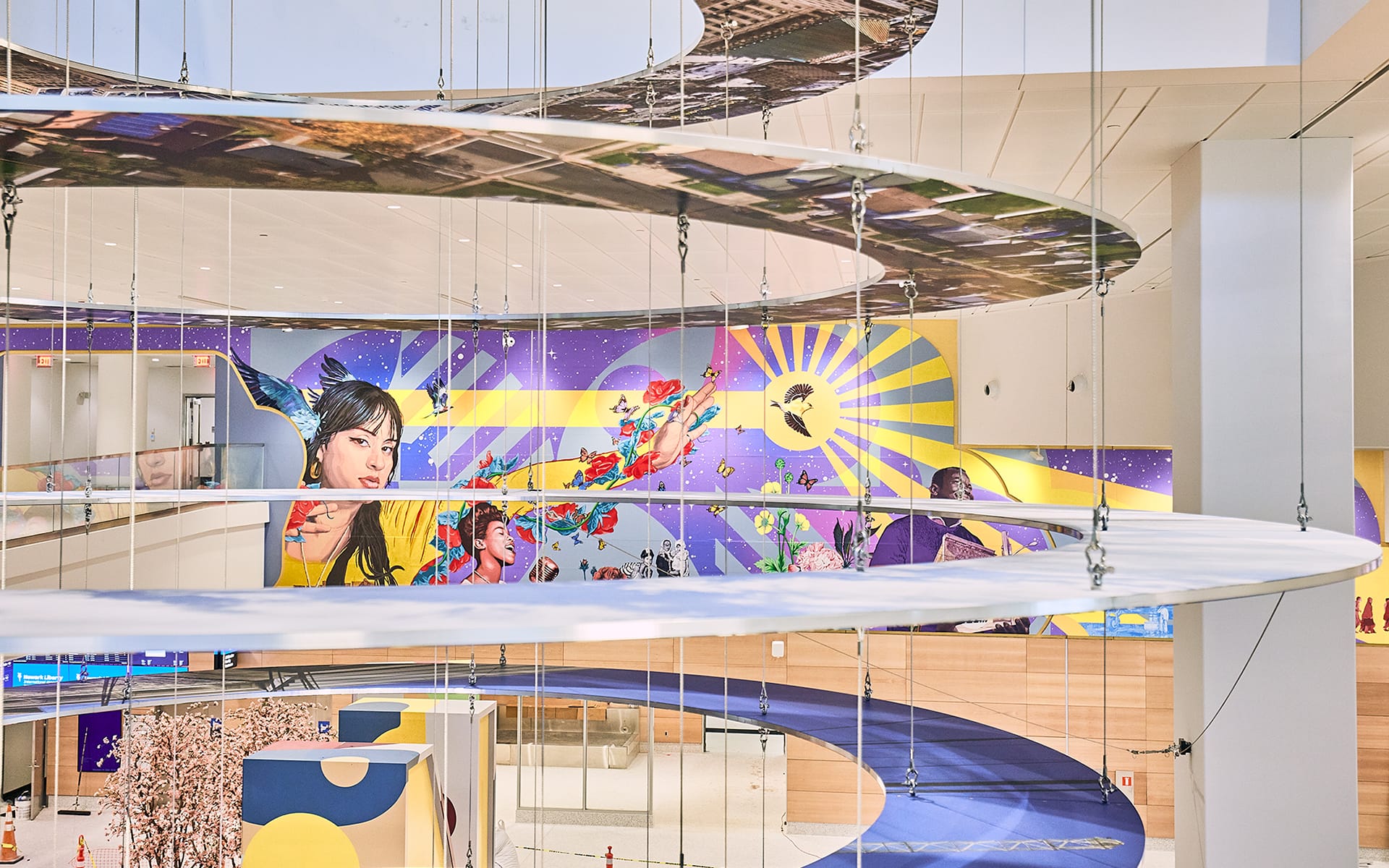 Colorful hanging spirals and vibrant wall mural in modern indoor space, featuring artistic portraits and abstract designs.