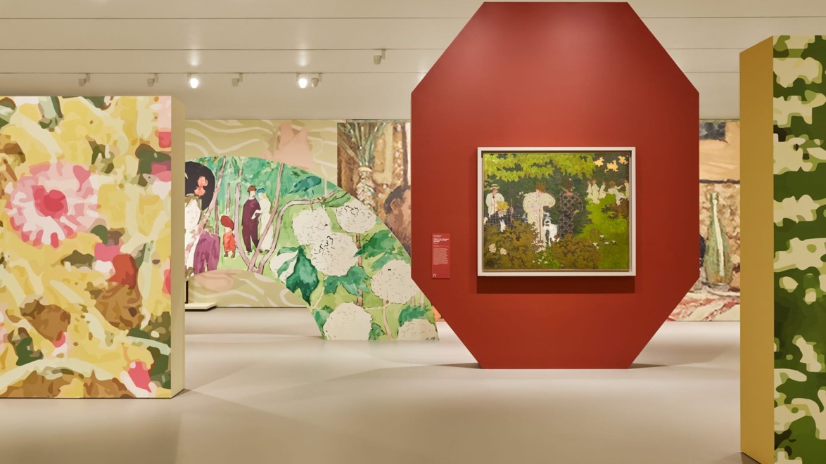 Art exhibition featuring several colorful paintings displayed on uniquely shaped walls in a modern gallery setting.