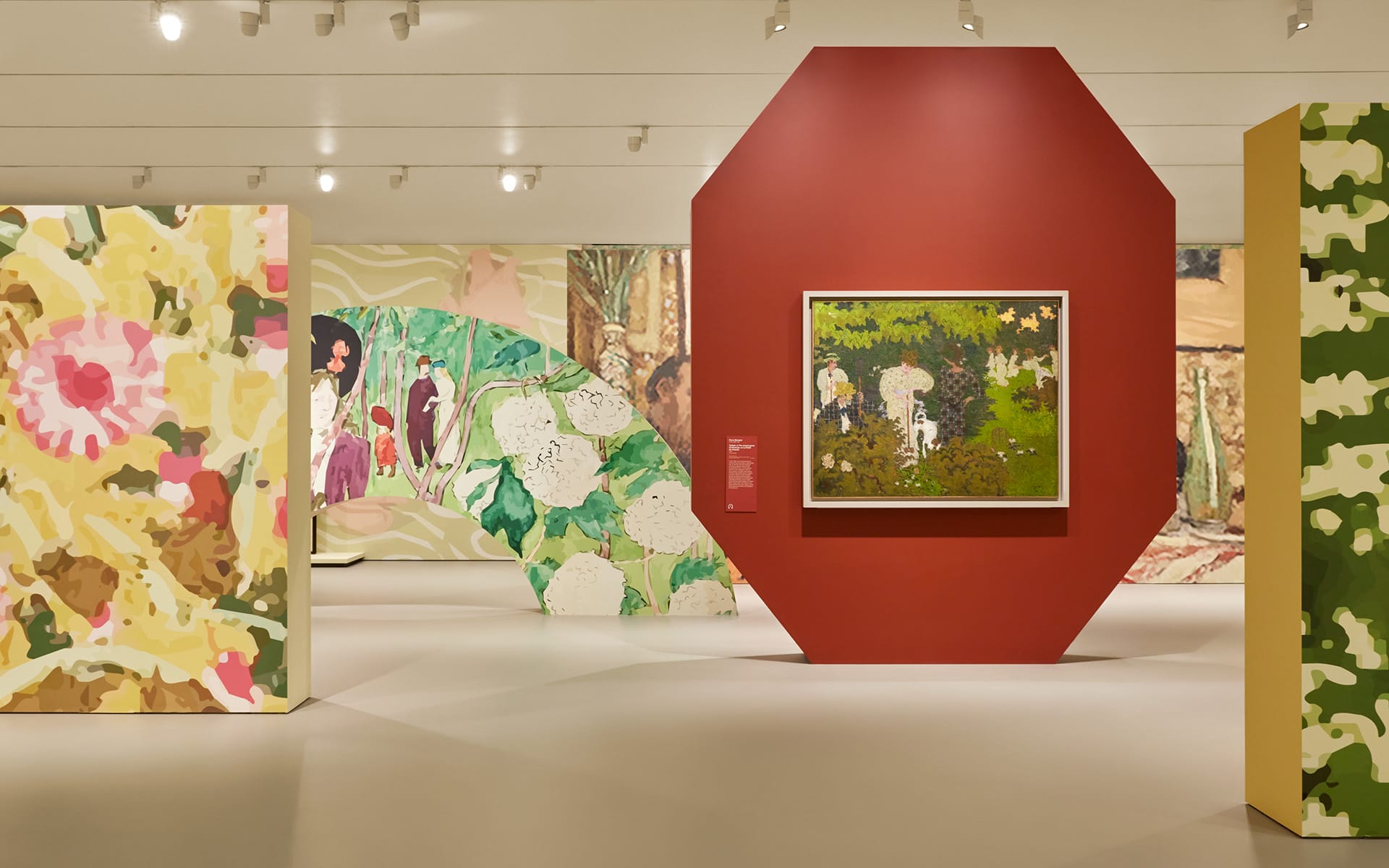 Art exhibition featuring several colorful paintings displayed on uniquely shaped walls in a modern gallery setting.