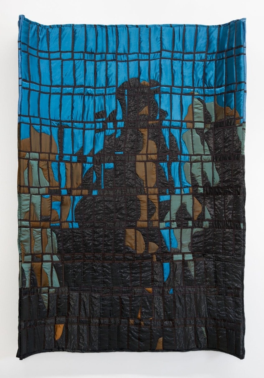 Colorful quilt with a geometric pattern featuring abstract shapes in blue, black, brown, and gray tones against a white background.