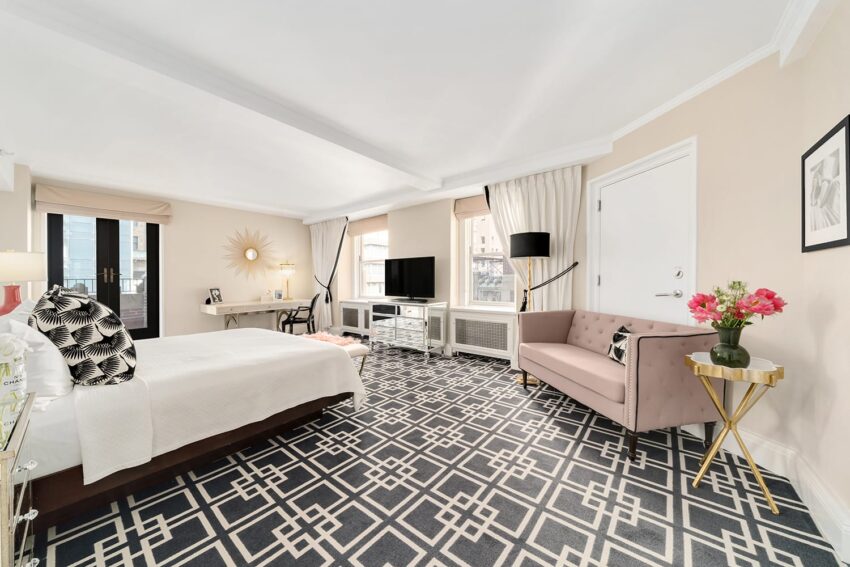 Stylish hotel room with geometric patterned carpet, modern furniture, large windows, and elegant decor elements.