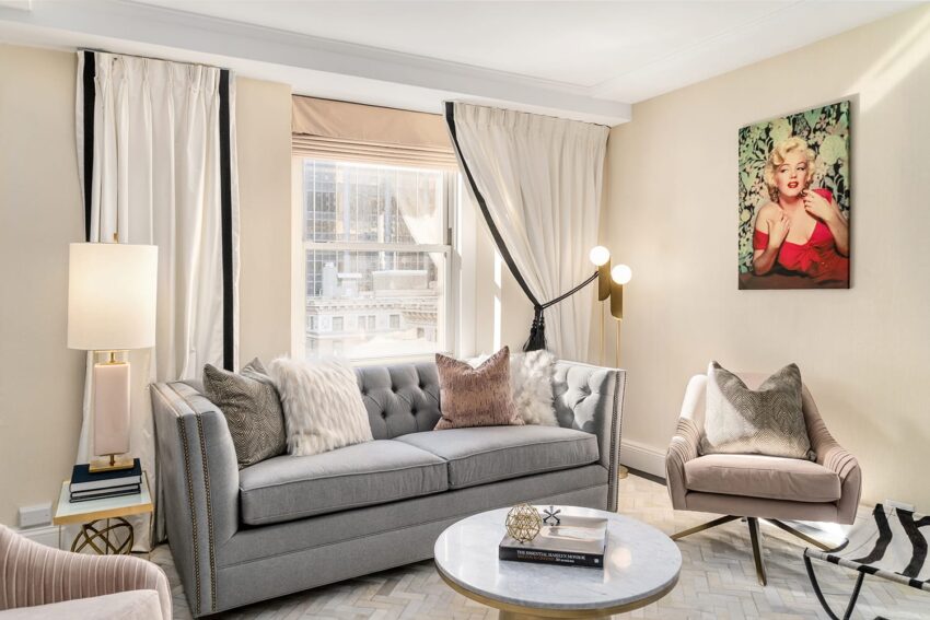 Elegant living room with gray sofa, modern lamp, armchair, artwork on wall, and large window with city view.