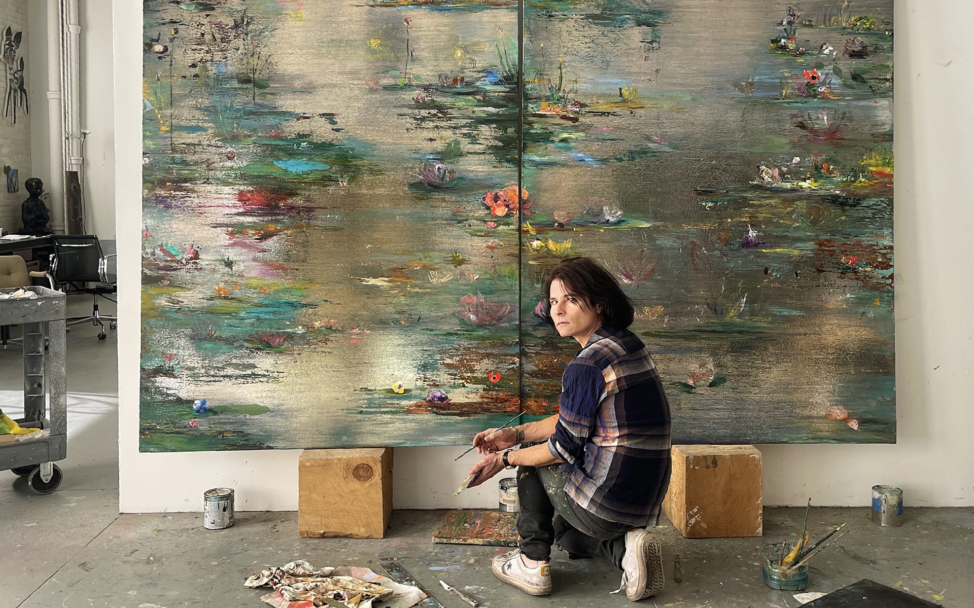 Artist working on a large, colorful abstract painting in a studio setting with art supplies scattered around.