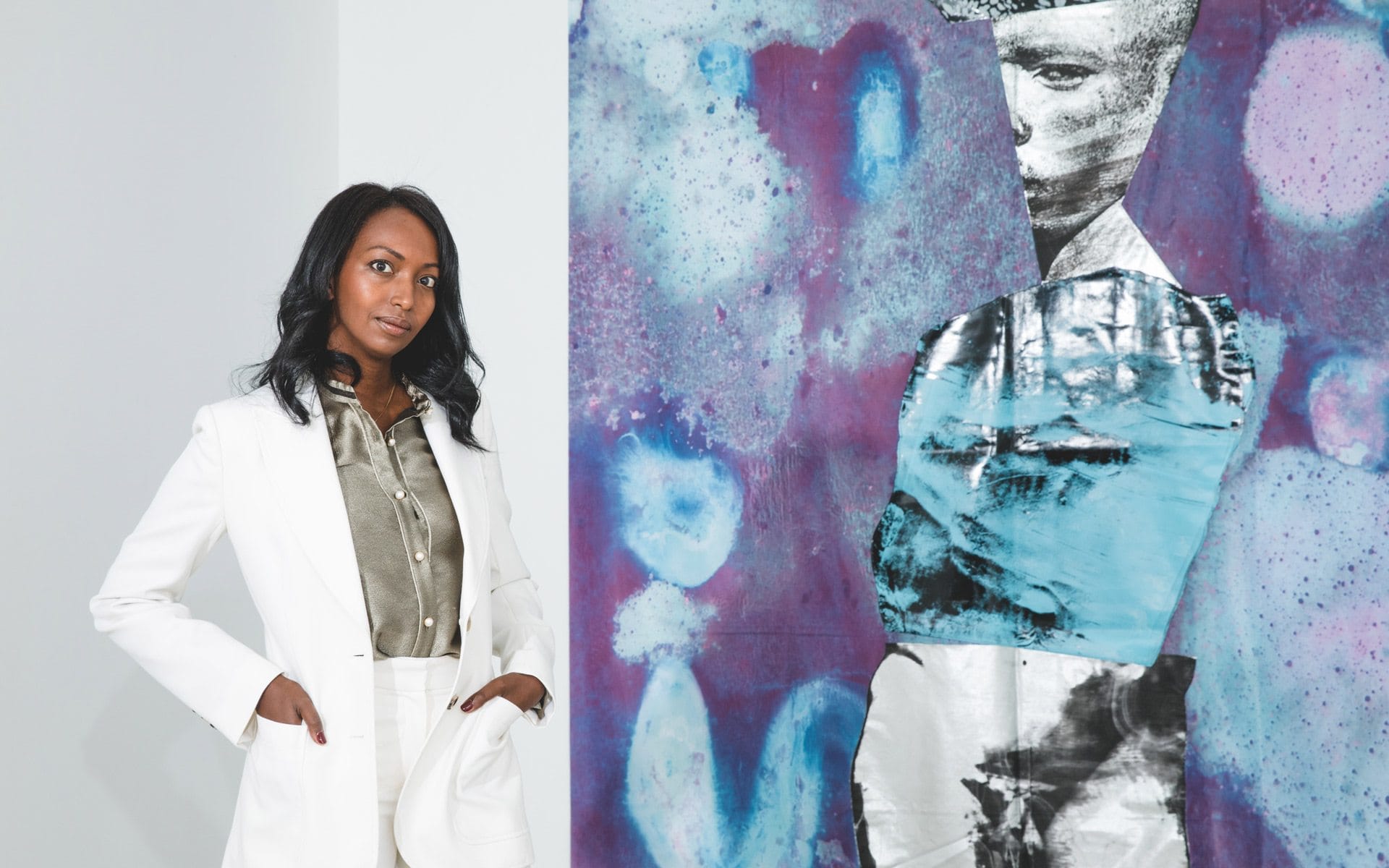 Woman in white suit standing beside abstract blue and purple artwork in a gallery setting.