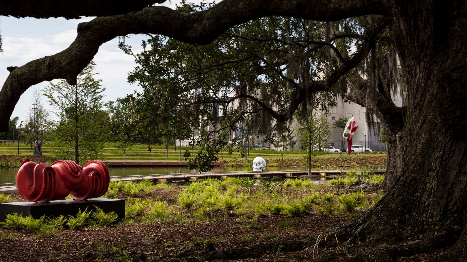 Sculptures in an outdoor art garden with trees and greenery, featuring a large red sculpture in the foreground.