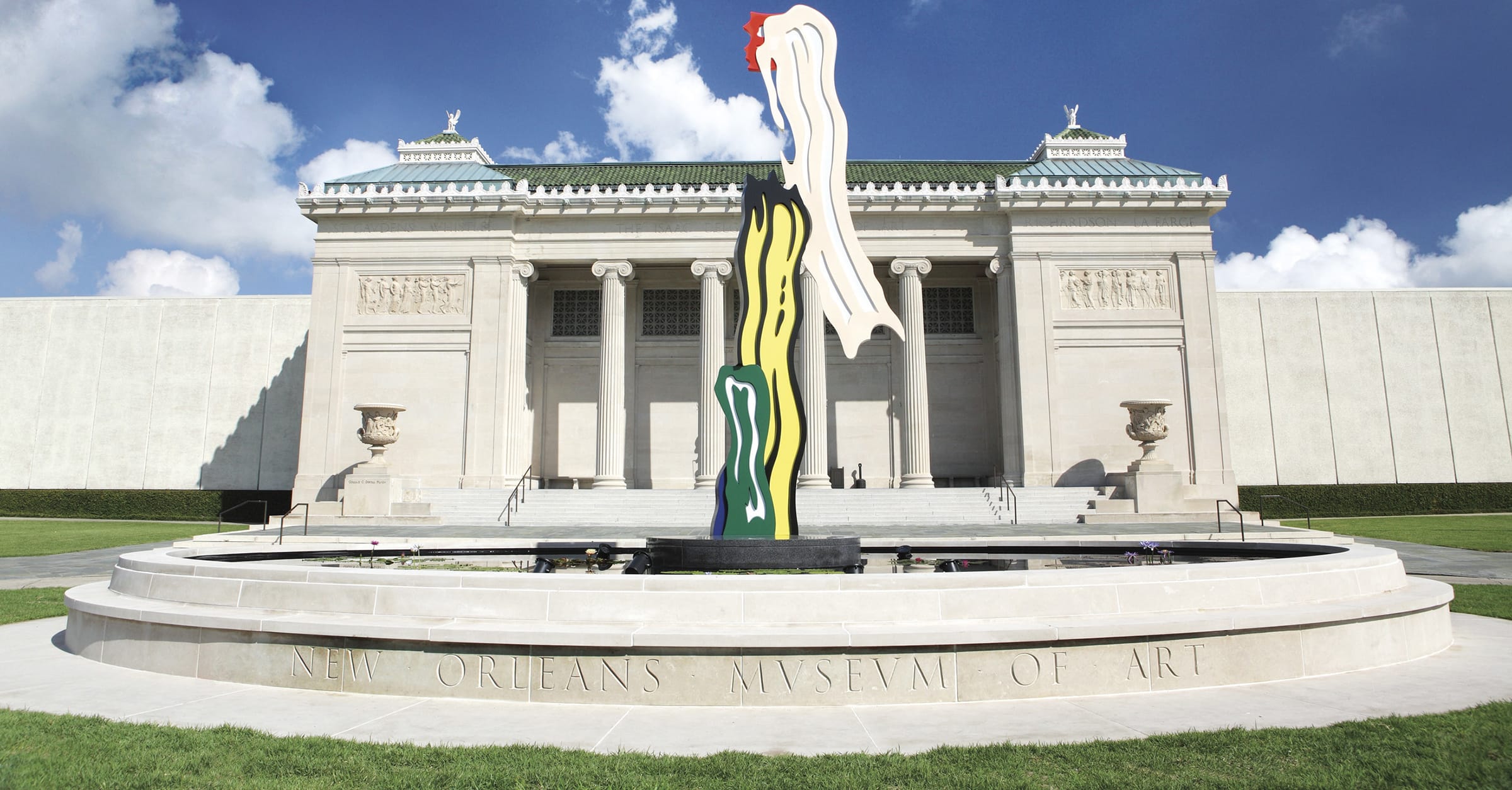 Entrance view of the New Orleans Museum of Art with a tall abstract sculpture in the foreground and a clear blue sky.