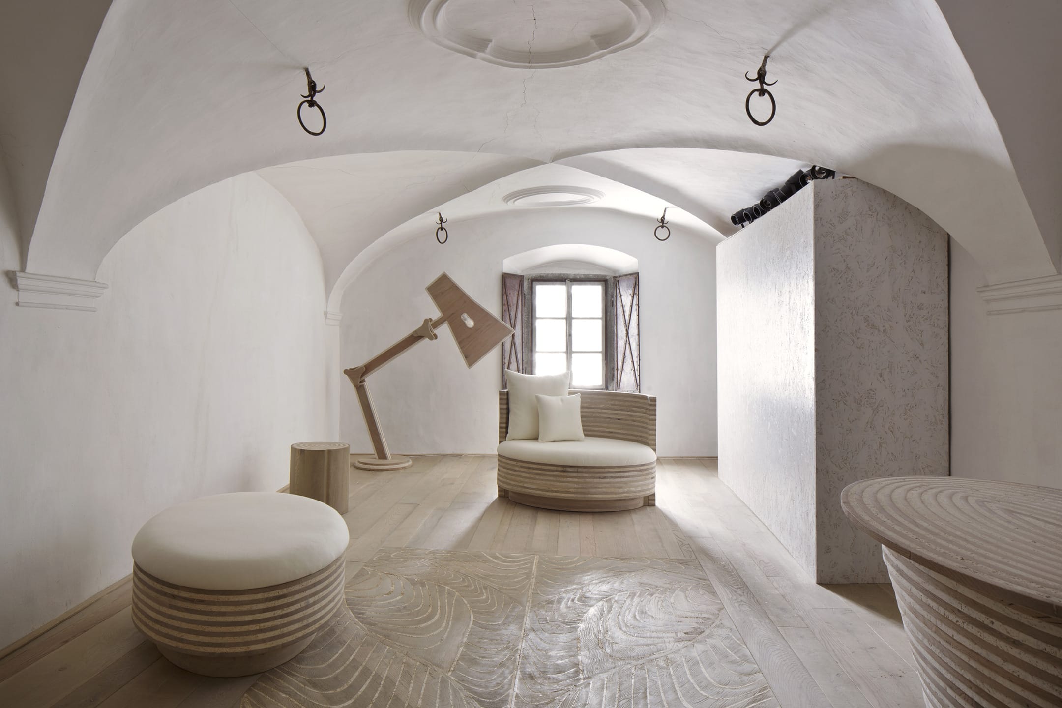 Minimalist room with curved ceiling, modern wooden furniture, large lamp, natural light from a window, and neutral colors.