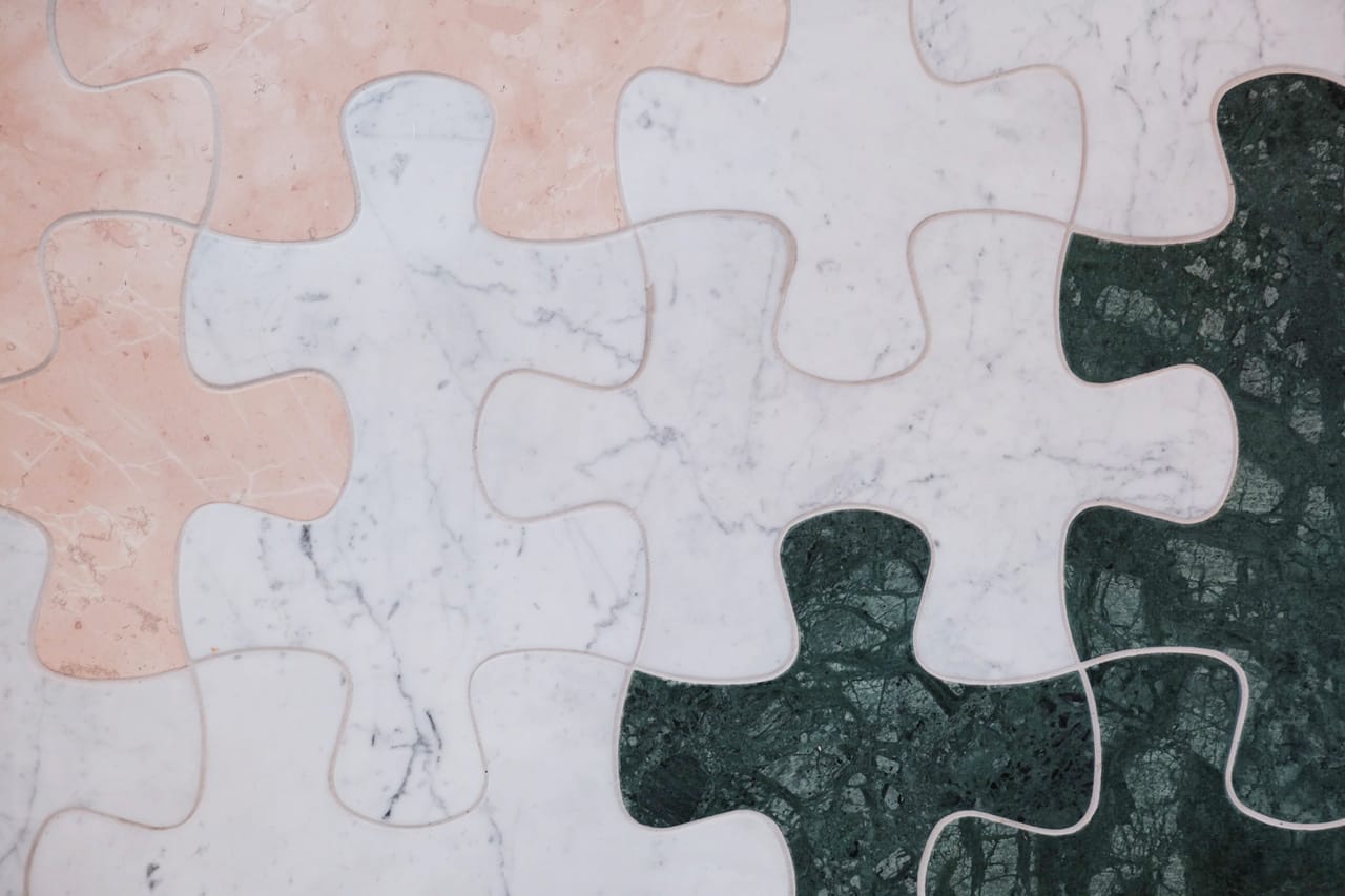 Close-up of interlocking puzzle pieces with marble textures in shades of pink, white, and green.