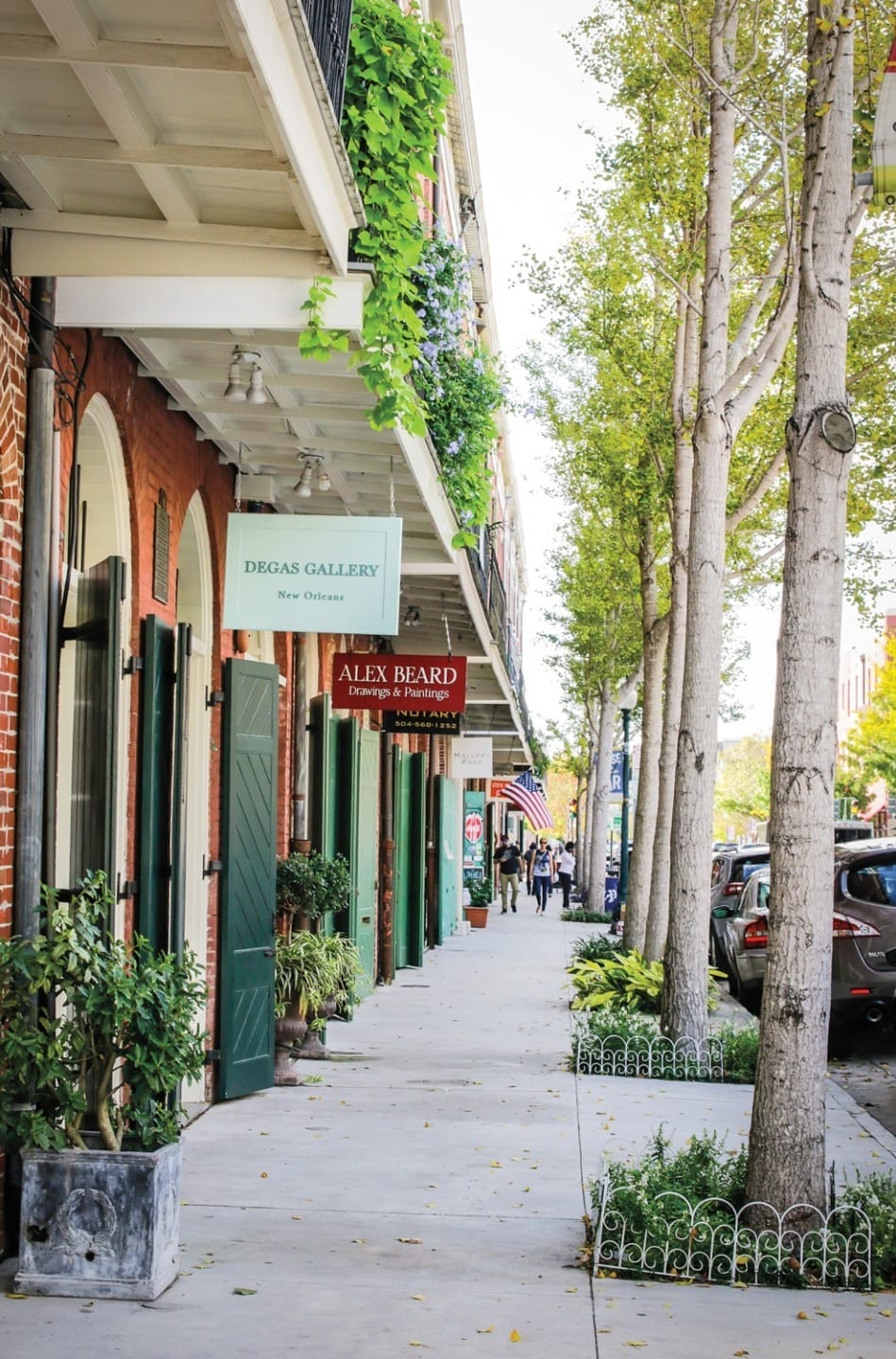 A picturesque street in New Orleans with trees and galleries, including Degas Gallery, lining a sunny sidewalk.