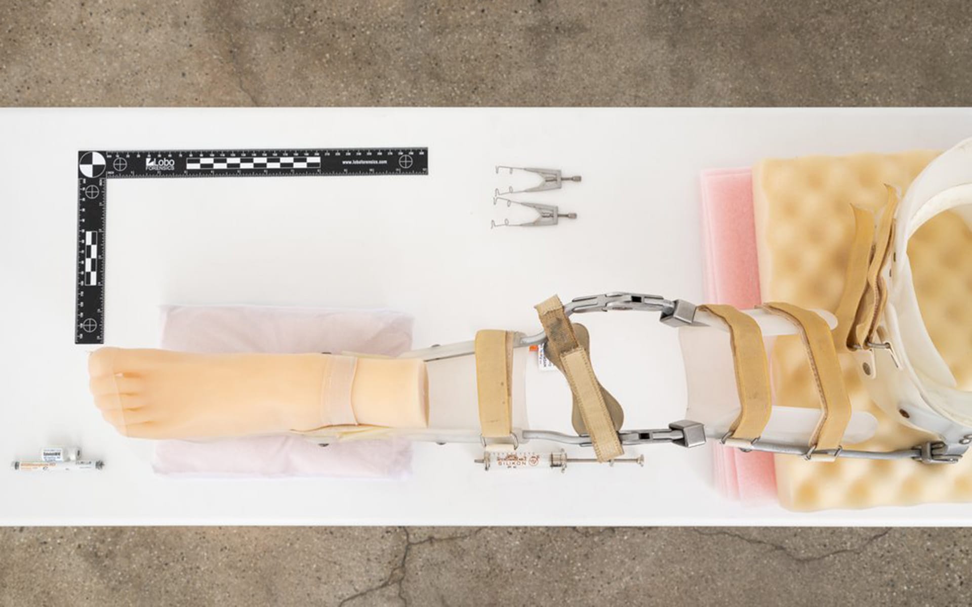 Prosthetic leg with adjustable components on a table, surrounded by measurement tools and padding.