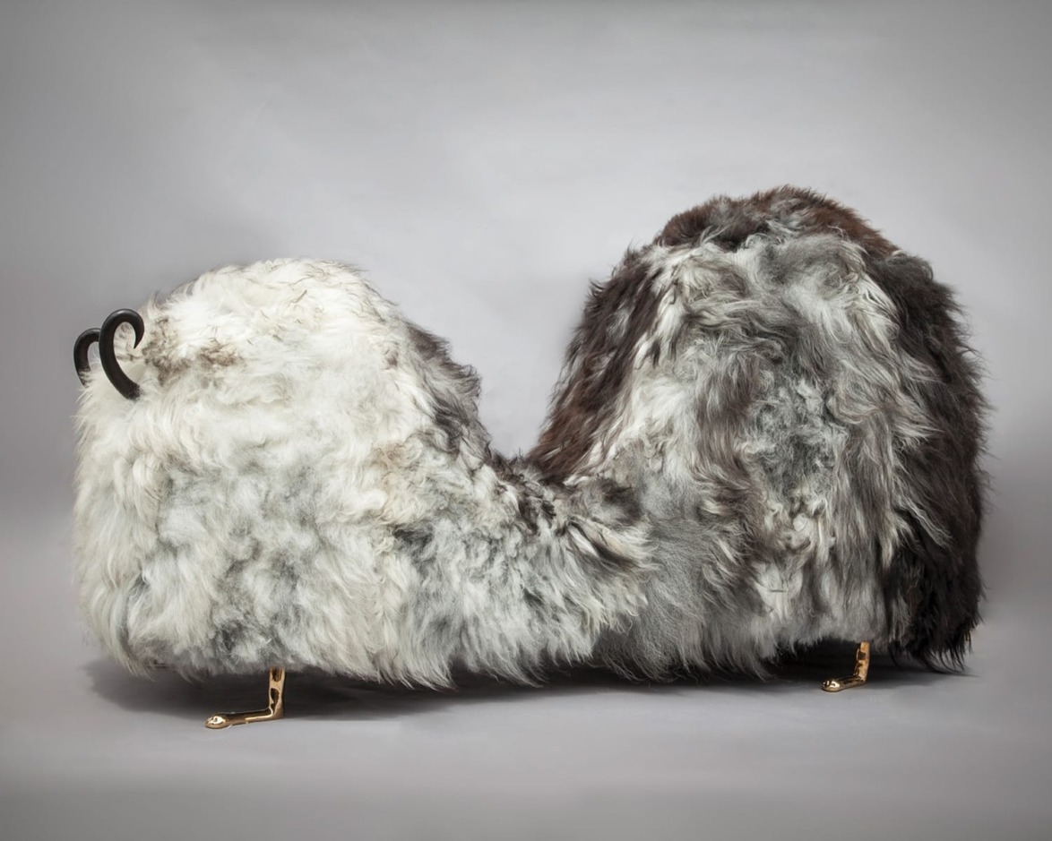 Curved, furry bench with gray and white fur texture and decorative metal legs against a neutral background.