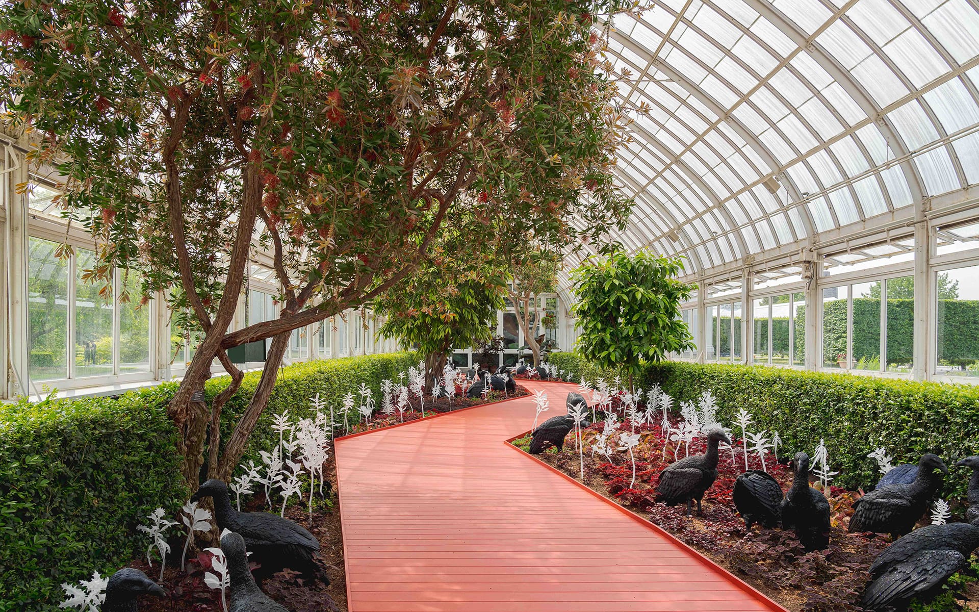 Colorful garden pathway with plants and sculptures inside a large greenhouse.
