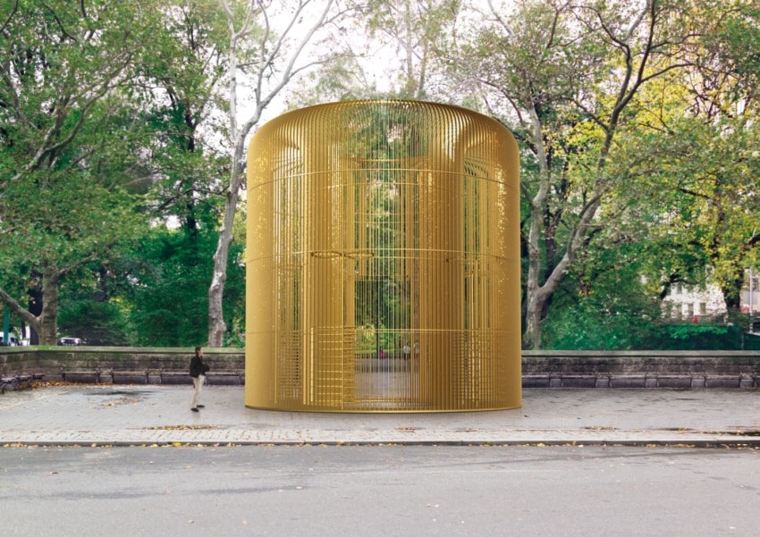 Golden cylindrical art installation in a park surrounded by trees, with a person walking nearby.