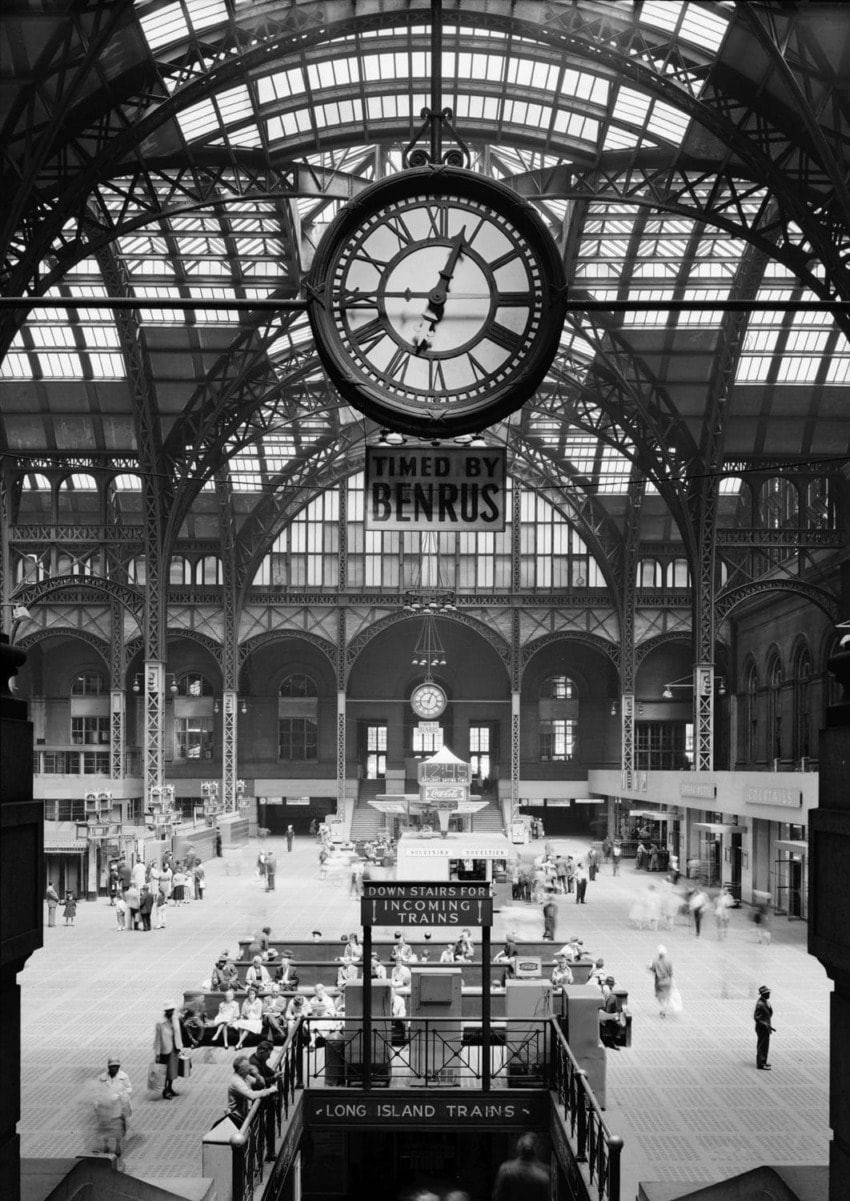 Historic interior of Penn Station with a large clock, arched windows, and travelers bustling through the grand hall.