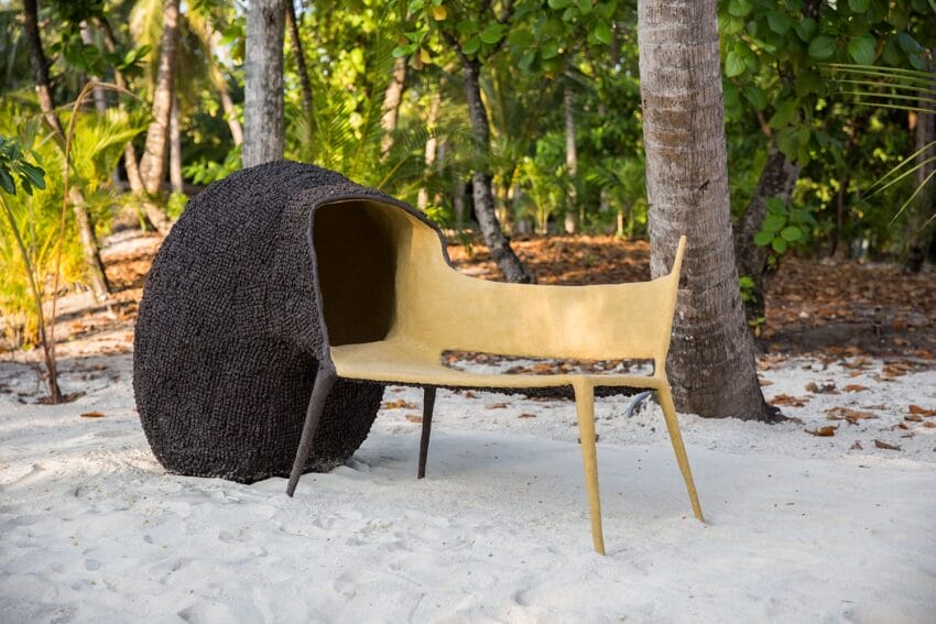 Unique lounge chair on sandy beach with lush green trees in the background