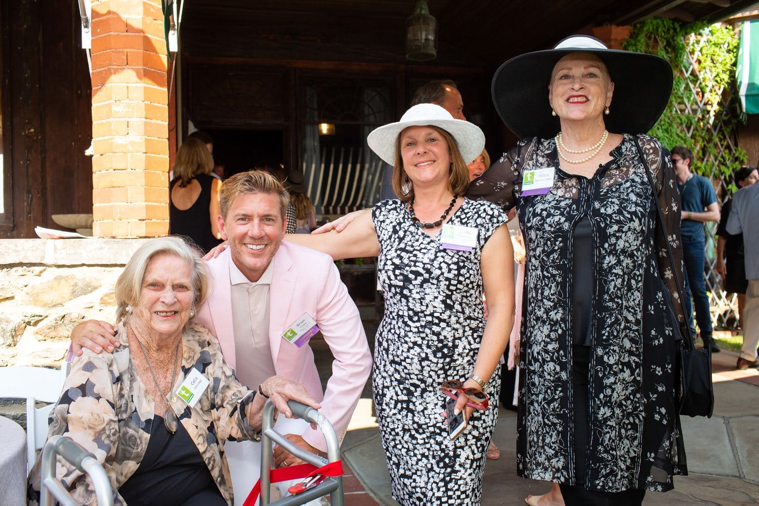 Group of four people smiling outdoors, with two women wearing hats and a man in a pink jacket.