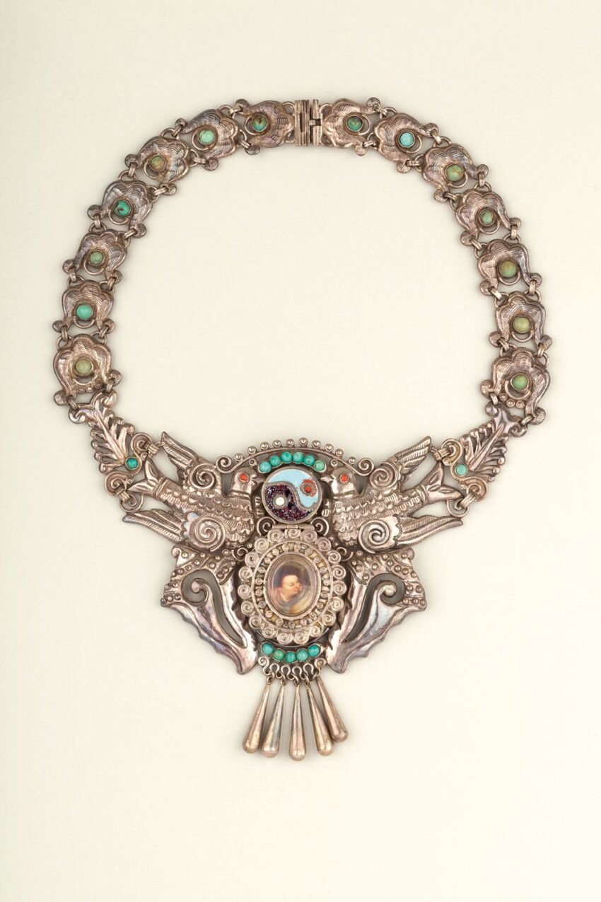 Intricate silver necklace featuring a central cameo and ornate decorations with turquoise accents on a light background.