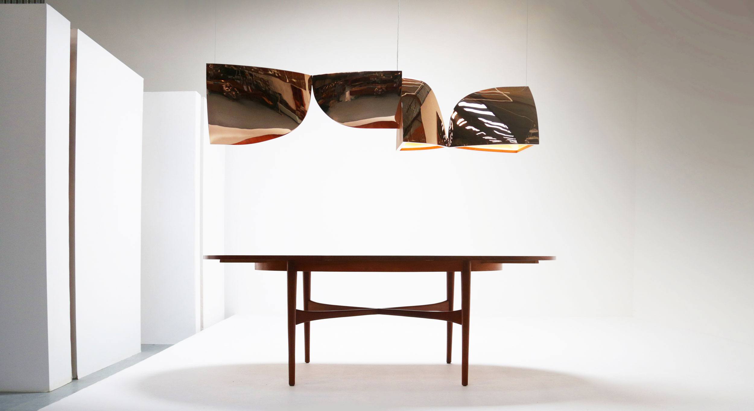 Modern wooden table under three curved metallic pendant lights in a minimalistic white room.
