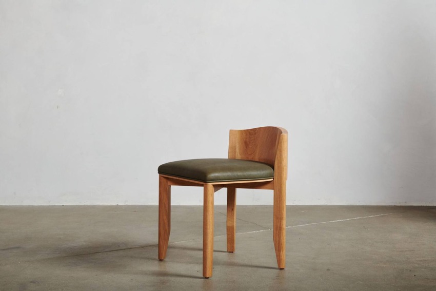 Wooden chair with a green cushioned seat in a minimalist setting on a concrete floor.