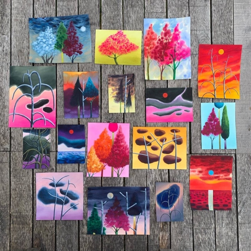 Colorful paintings of trees displayed on a wooden surface. Each painting features vibrant, abstract tree designs.