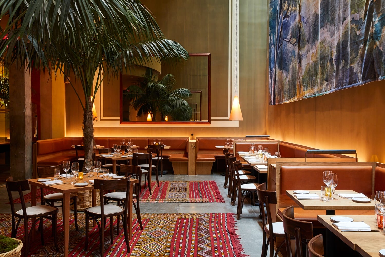Stylish restaurant interior with colorful rugs, wooden tables, leather seating, and large indoor plants.