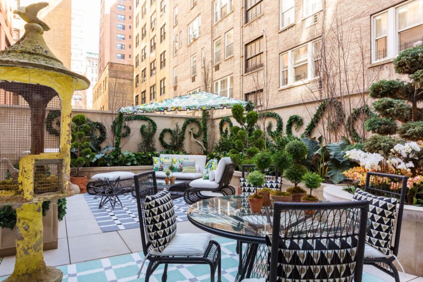 Outdoor patio with black and white furniture, green plants, patterned tiles, and city buildings in the background.