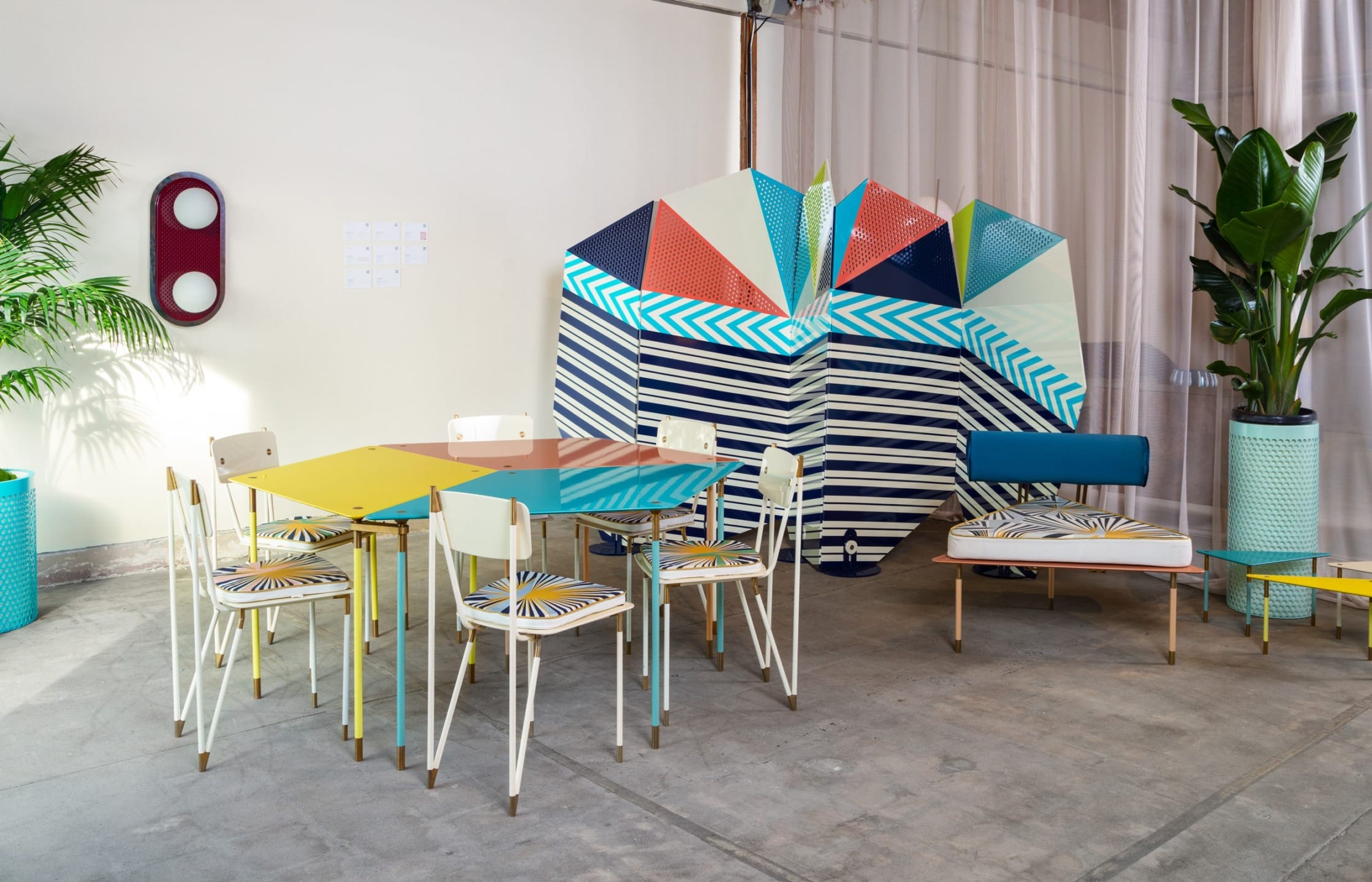Colorful modern dining area with geometric patterns, plants, and a unique wall art installation in a stylish interior setting.