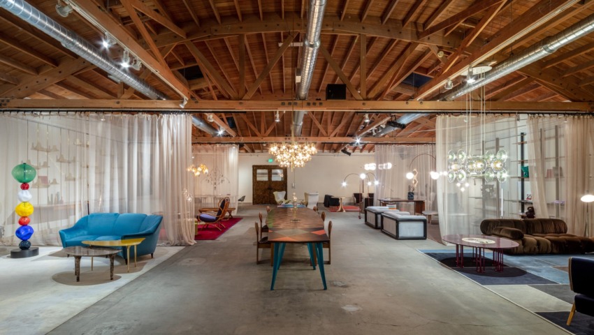 Spacious modern lounge with eclectic furniture, vibrant lighting fixtures, and a high wooden ceiling.