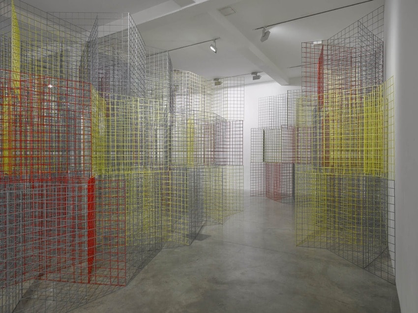 Colorful grid-like mesh panels arranged in a spacious modern gallery, creating an abstract and geometric installation.